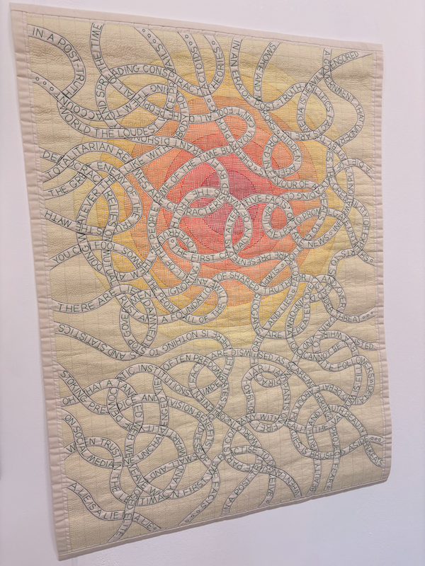 a quilt with a red centre gradually fading to cream as it moves away from the centre. on top are tangled chains of words saying things like - democracy relies on mutual trust and a foundation of shared truth or it is under threat - stoking prejudice and division benefits a small and closed elite - and many other phrases