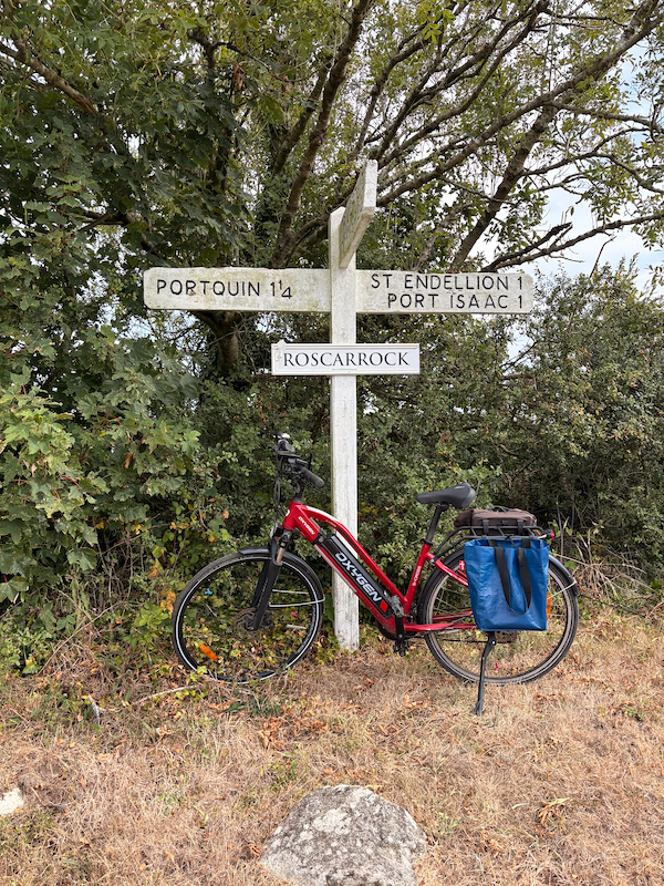 My bike in front of a sign post labelled Roscarrock, It’s 1 1/4 miles to Portquin, and a mile to either St Endellion or Port Isaac