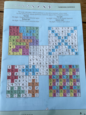 A completed Samurai Sudoku puzzle, consisting of five interlinked sudoku grids, with various numbers filled in and some cells coloured. Instructions for additional constraints on the four corner puzzles are written at the top.
